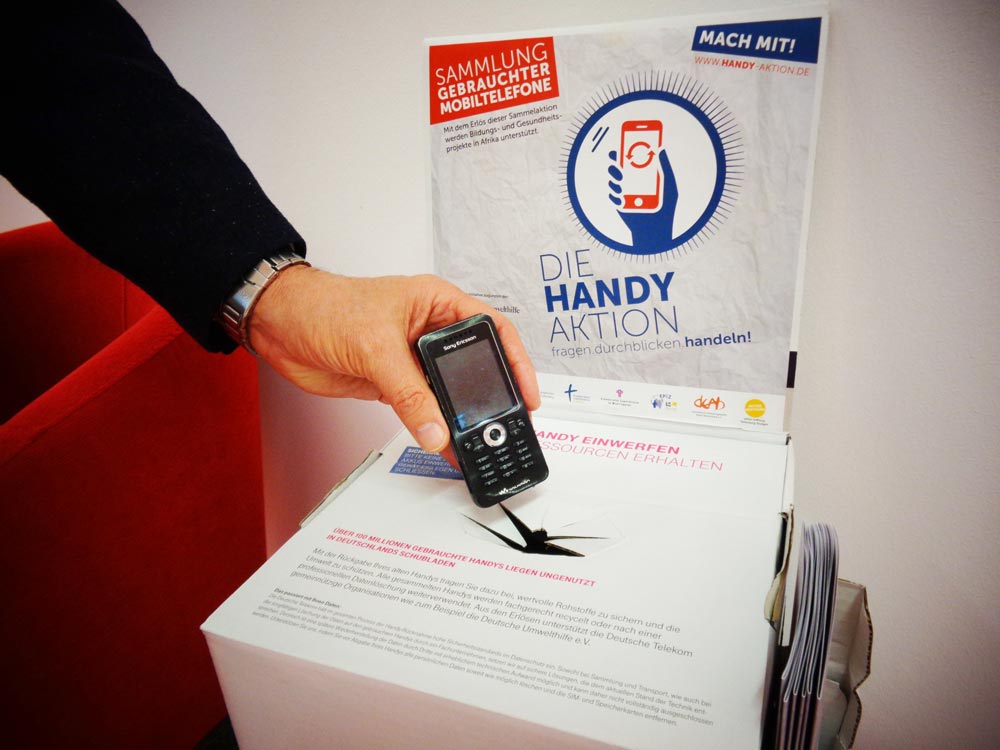 Handysammelbox der Handy-Aktion Bayern – Einwurf eines Alt-Handys Smartphone für die Handy-Sammelaktion